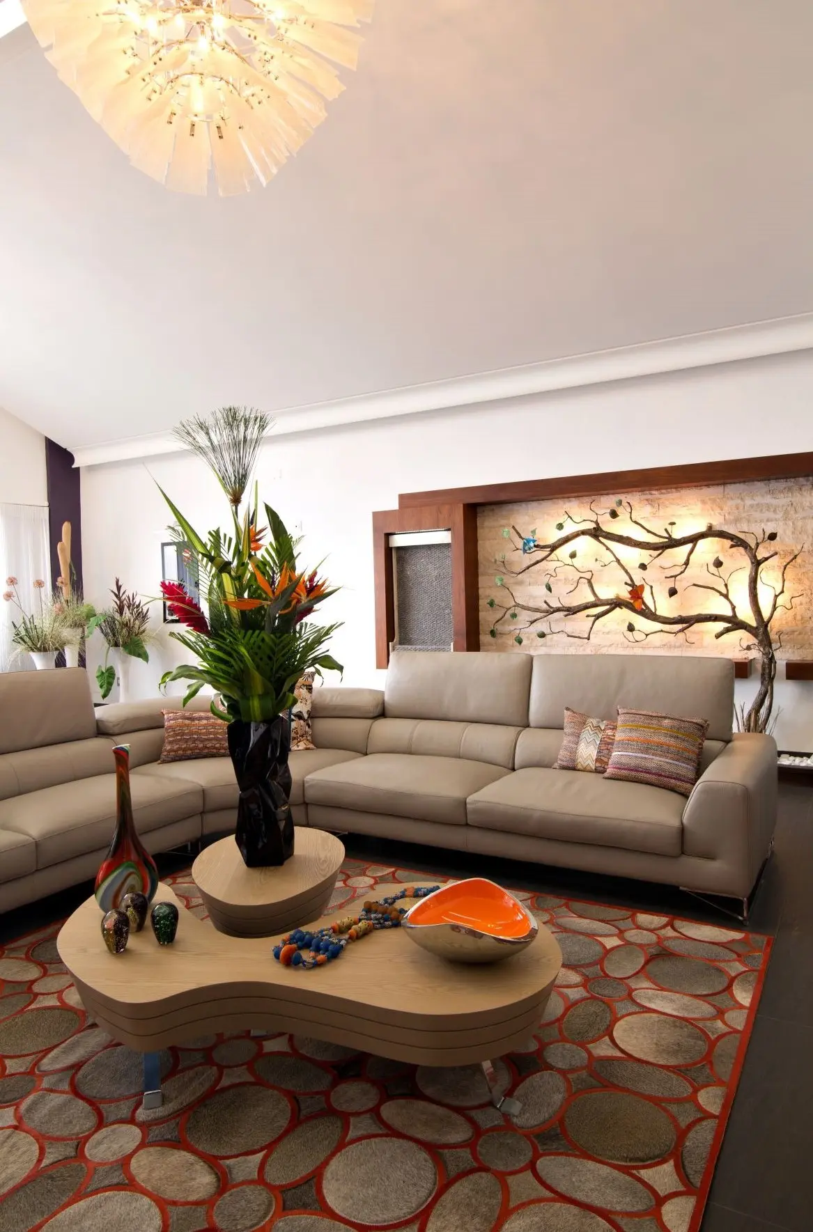 Living room with sofa, table and rug in the center. Tree sculpture in the background