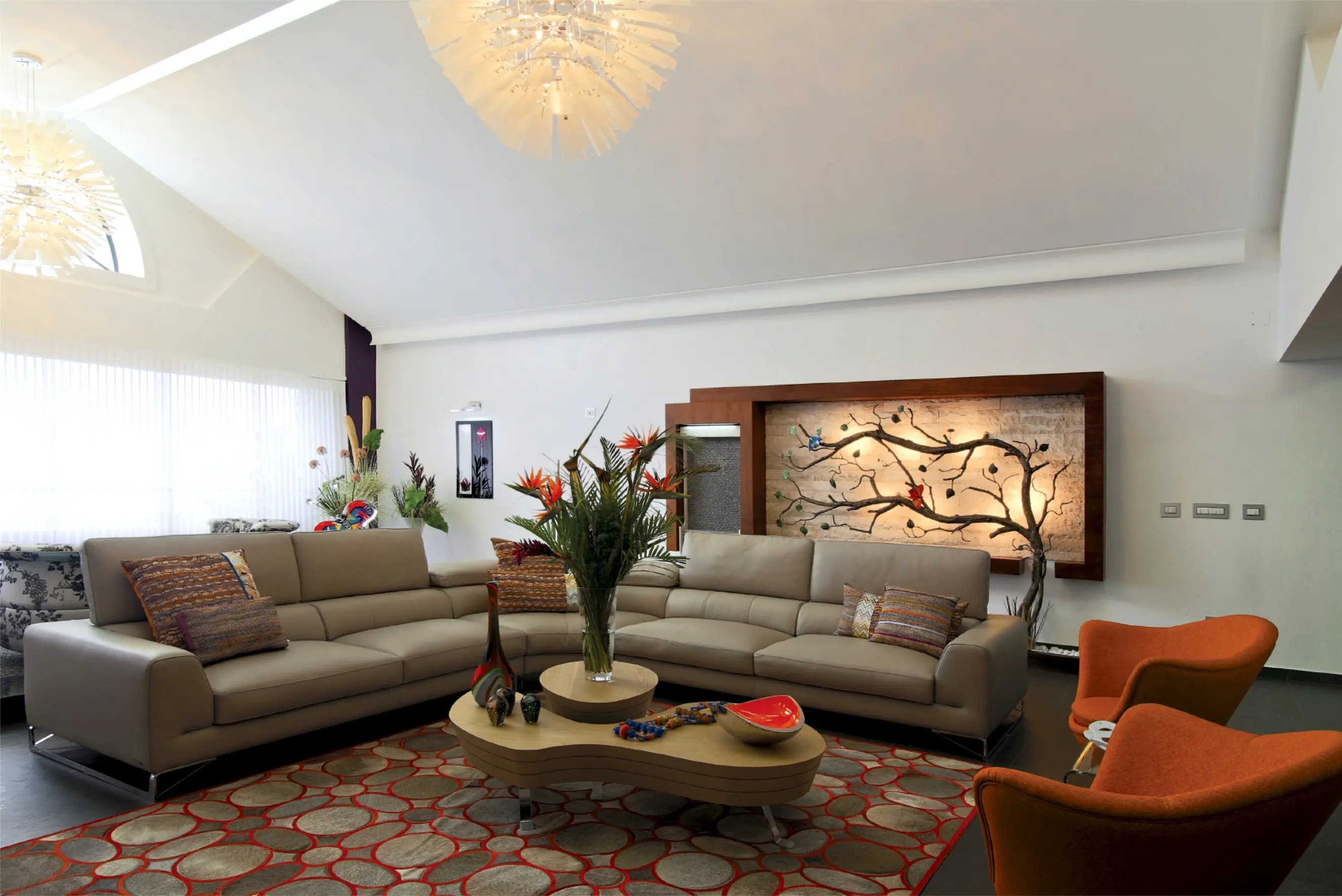 Living room with sofa, table, rug and orange chairs. Tree sculpture in the background