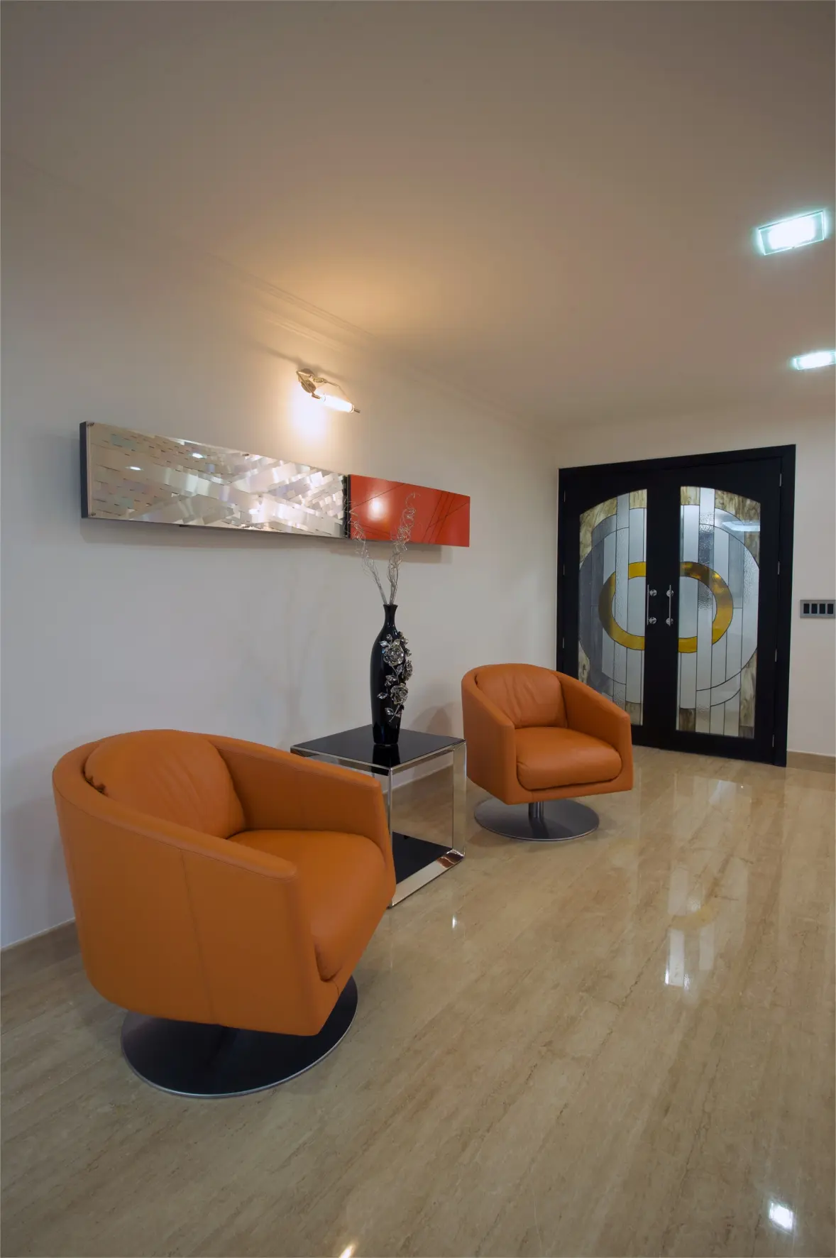 2 orange armchairs with table in the middle and wall sculpture